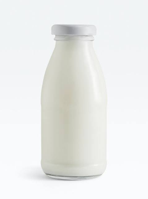A simple product shot of a white glass milk bottle with a silver cap, filled with milk, shown against a plain white background.
