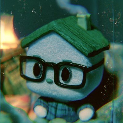 A plush doll with a green roof-shaped head, black glasses, and blue pajamas sits in soft focus, suggesting a whimsical new addition to a community. The caption "Welcome @MEADGod!" pairs with the cozy, inviting aesthetic of the stuffed toy to greet the new member.