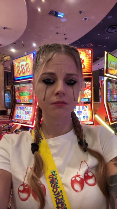 The image features a woman wearing a white t-shirt that has red cherries printed on it, along with a yellow ribbon around her neck. She appears to be sad or upset as she looks down at something off camera. The caption of the image reads "crypto bros with 0.01 BTC when Michael Saylor sells 1/10000 of his BTC". This suggests that the woman might have invested some money in cryptocurrency, and if so, how much?