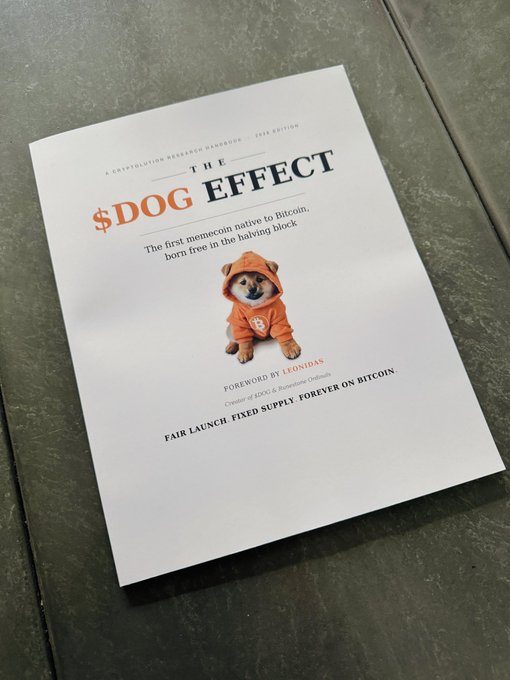 A book titled 'THE $DOG EFFECT - The first memecoin native to Bitcoin, born free in the halving block' featuring a Shiba Inu dog in an orange hoodie, with text 'FAIR LAUNCH FIXED SUPPLY FOREVER ON BITCOIN' and 'Foreword by Leonidas'.