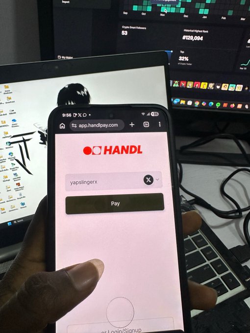 A hand holds a smartphone displaying the app.handlpay.com login page with username 'yapslingexx', in front of a laptop screen showing analytics dashboards.