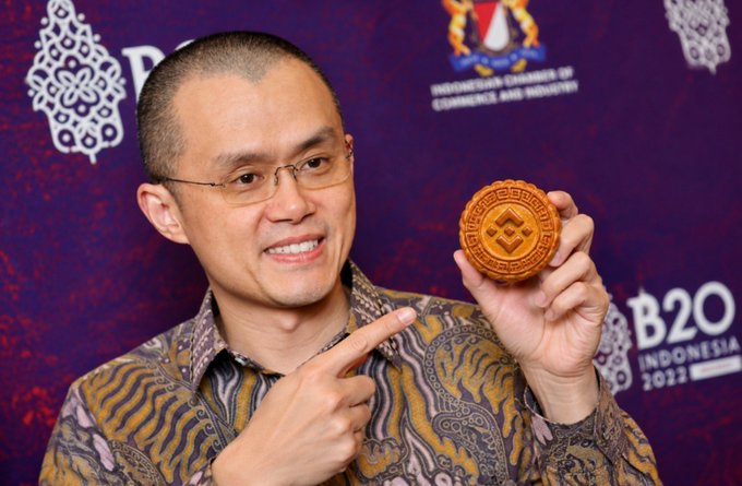 Photo of a man wearing glasses and a patterned batik shirt, holding up a B20 Indonesia 2022 commemorative coin at a B20 Indonesia 2022 event backdrop.