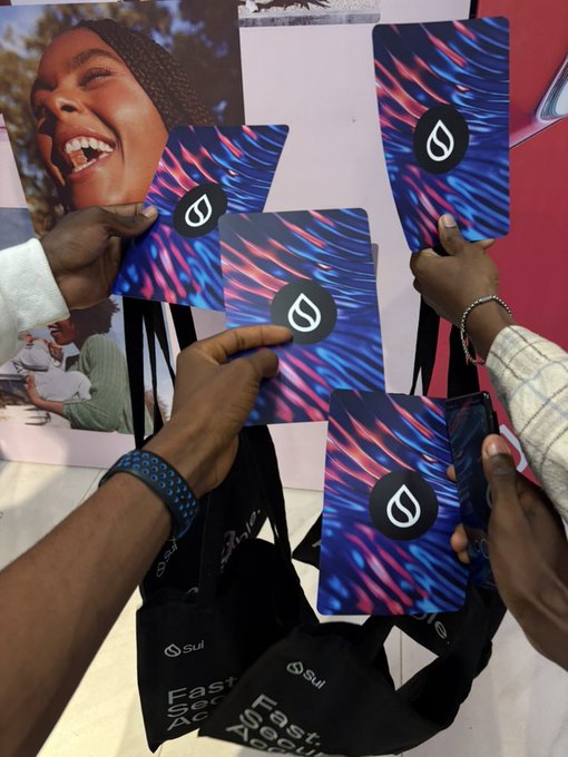 The image shows a group of people holding up five business cards, each card featuring a unique design or logo. One person's hand is holding two cards with a blue and red design, while another person holds three cards with a purple and black design. The remaining two individuals hold four cards each with different designs. The post in the image reads "Sui is the future", which suggests that these business cards could be related to a company or event named Sui.
