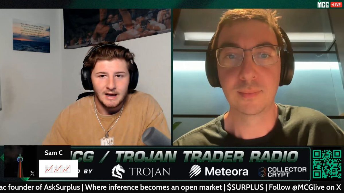 The image shows a man wearing headphones, sitting at a desk with another person behind him who appears to be talking into a microphone or headset. The two individuals are engaged in a conversation, possibly discussing a podcast or radio show they are hosting together. In the background of the image, there is text that reads "SURPLUS launched through @bankrbot with zero involvement from @mac_eth in the beginning He decided to adopt it when people actively made introductions and pursued collaboration opportunities on the project' s behalf A significant percentage of total system-wide $DIEM usage".