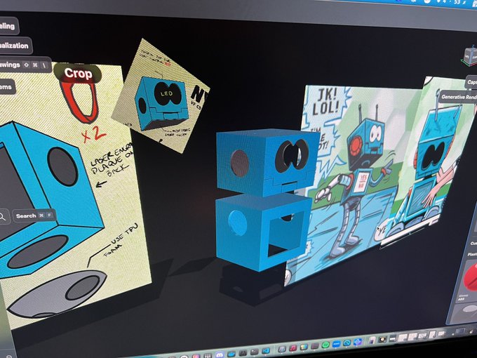 A computer monitor displays a 3D modeling workspace showing two stacked blue cubes with faces, alongside digital sketches of similar robot characters and handwritten notes like "Crop" and "CRACK ENAMEL PAINT? OH".