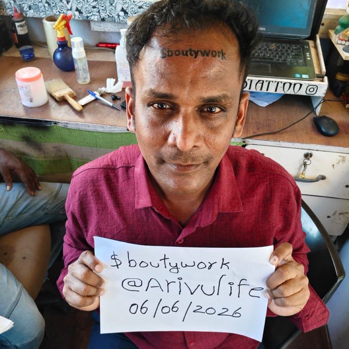 A tattoo of a man's forehead that says "bouttywork" on his head, with a "Memecoin" sign below. The image also includes a caption saying "I love this I love Memecoin Memecoin have come to stay Memecoin will never die".