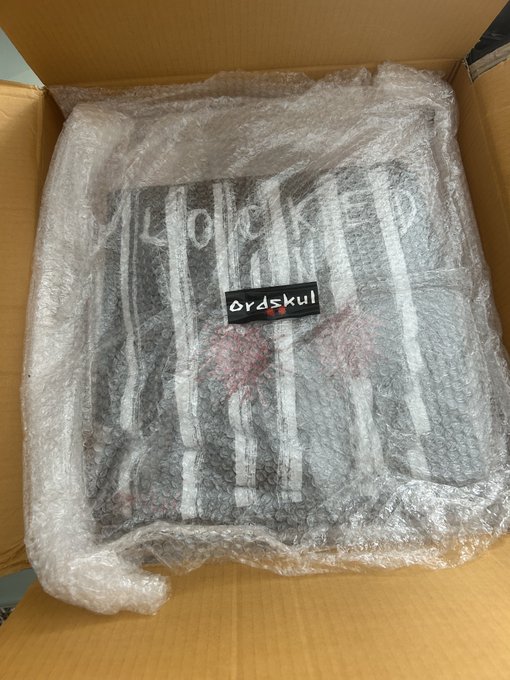 An open cardboard box containing a striped black and white item wrapped in bubble wrap with a label reading 'Grdskul'.