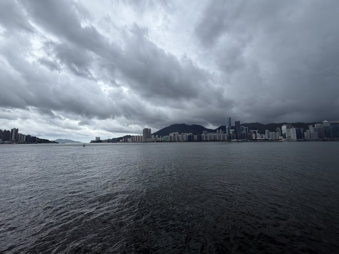 The image shows a view of a city skyline with tall buildings, including one that appears to be a skyscraper, against an overcast sky. The water below has dark waves, suggesting choppy conditions or possibly rough seas. The photo seems to have been taken from across the water, providing a panoramic perspective of the cityscape and its surroundings.