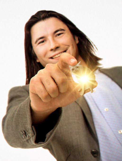 A young man with long hair smiles triumphantly while pointing at a small white figurine (resembling a mouse or toy) that emits a bright light from his outstretched hand, capturing the meme-like "My precious" pose with Gollum-esque intensity.