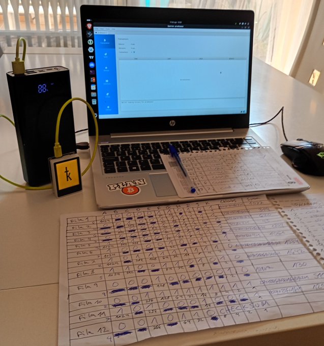 A handwritten paper spreadsheet details Bitcoin transaction tracking across multiple "Blk" (block) entries with dates, amounts, and checkmarks, while an HP laptop in the background runs the Bitcoin Core dashboard—a low-tech, pen-and-paper method for organizing crypto data. The accompanying note emphasizes that Bitcoin's decentralization philosophy embraces manual, printer-free record-keeping as a form of financial sovereignty.