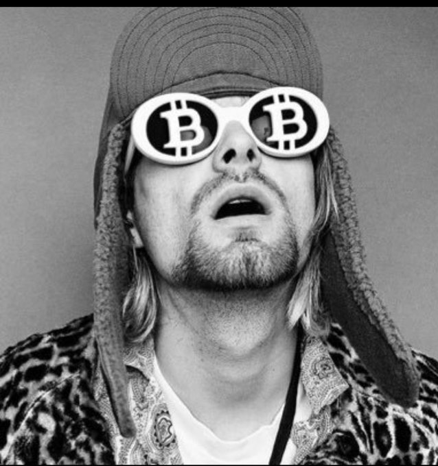 A black-and-white photo of a man wearing a cap and 'Bitcoin' logo sunglasses, looking upward.