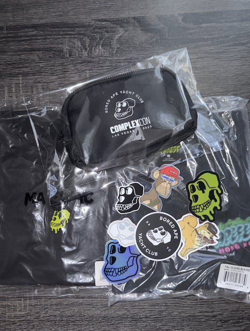 The image shows black "Bored Ape Yacht Club" and "ComplexCon 2022" branded merchandise, including a small zip pouch and a sticker pack featuring colorful ape skull designs and a "Bored Ape Yacht Club" sticker, all still in clear plastic packaging. The "Bored Ape" branding aligns with the post's shoutout to @KaijuTheApe, suggesting this is a bundle of ape-themed collectibles received from that account.