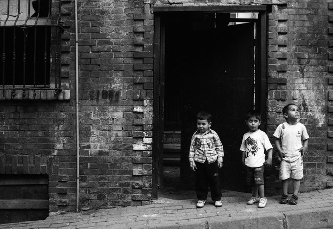 A black-and-white photograph of three young boys standing in the doorway of a weathered brick building.