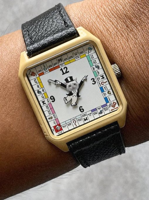 A wristwatch featuring a Monopoly-style game board dial with the classic "Rich Uncle Pennybags" mascot is shown on a wrist, playfully mirroring the "$CASHCAT" token's board game theme referenced in the post about its early momentum on Robinhood Chain.