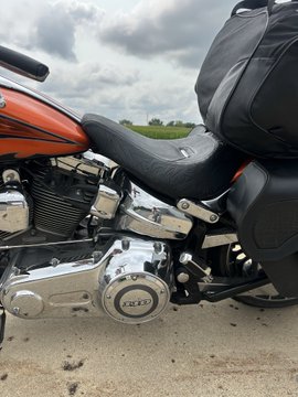 A close-up side view of an orange Harley-Davidson motorcycle showcasing its chrome engine with a "103" emblem visible on the primary cover, paired with a black leather seat. The caption references "110" (likely referring to cubic inch displacement), while the image actually shows the 103 cubic inch V-twin engine that powers this bike.