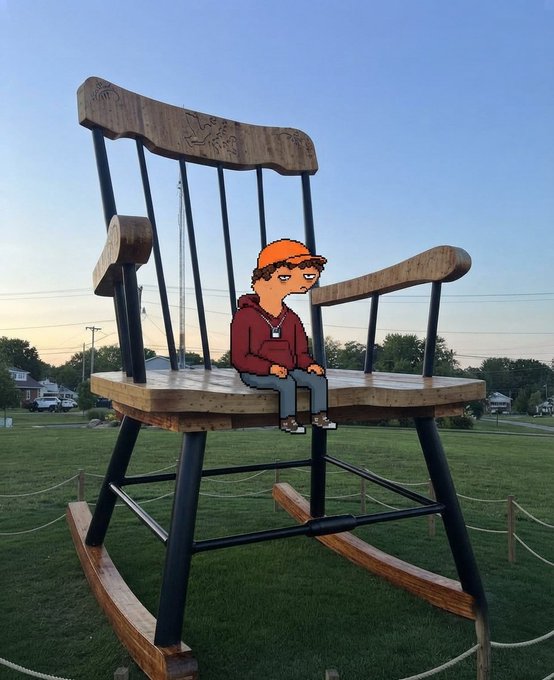 A photo of a giant wooden rocking chair displayed on a grassy field at sunset, with an animated cartoon character wearing an orange beanie and red hoodie digitally placed sitting on the chair's seat.