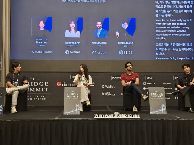 A panel discussion at 'THE BRIDGE SUMMIT' featuring four speakers on stage, with a screen displaying moderator Mark Loo and speakers Gemma Shin (Ecosystem Lead, Mantle), Nakul Gupta (COO, Multipli), and Blake Jeong (CEO, IO.ST).
