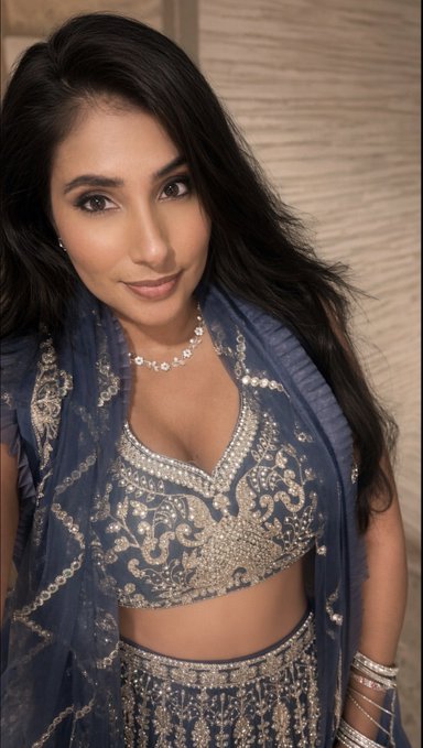 A woman with long dark hair wears an intricately embroidered blue lehenga choli with silver detailing and a matching dupatta, accessorized with a diamond necklace.