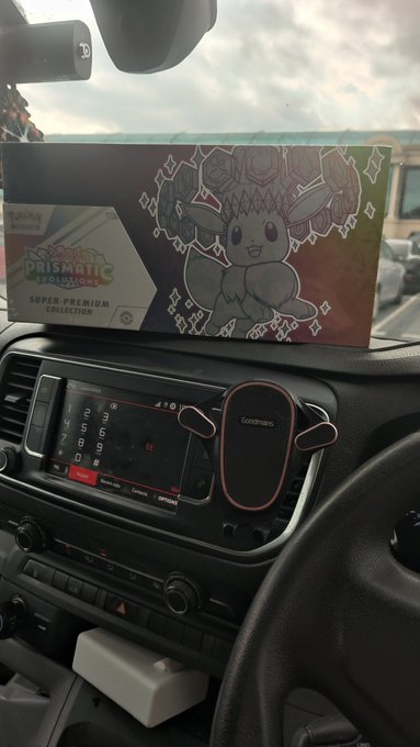 A Pokémon Trading Card Game Prismatic Evolutions Super-Premium Collection box sitting on a car dashboard.