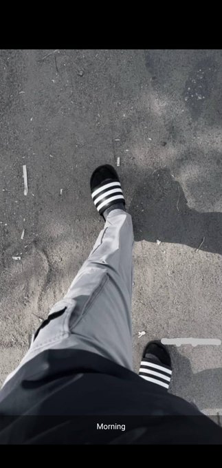 A black and white first-person view shows feet in Adidas slides walking on cracked asphalt, with a text caption 'Morning' at the bottom.