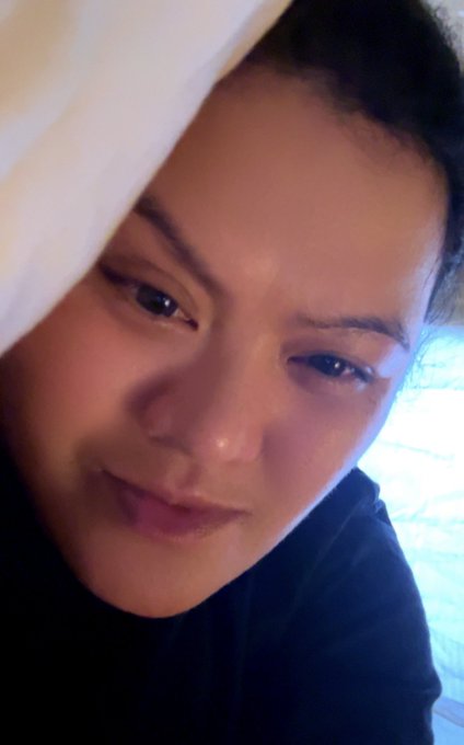 A woman wearing a white towel wrapped around her head lies down, appearing relaxed as she poses for a close-up selfie. Her expression ties to the post's giveaway celebration, where her claim of winning aligns with the user's surprise candy win announcement.