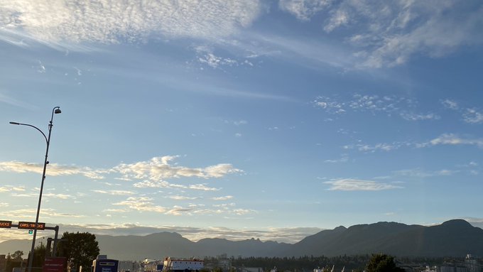 A scenic landscape photo featuring a blue sky with wispy clouds, distant mountains, and a street lamp, with a partially visible sign reading 'AGENCY CAMPUS CR...'.