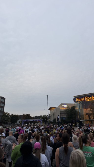 A large crowd gathers under an overcast sky outside the Hard Rock building for what appears to be a 10/10 anniversary race, with a starting arch visible in the distance—though the packed turnout somewhat contradicts the caption's claim of low attendance.