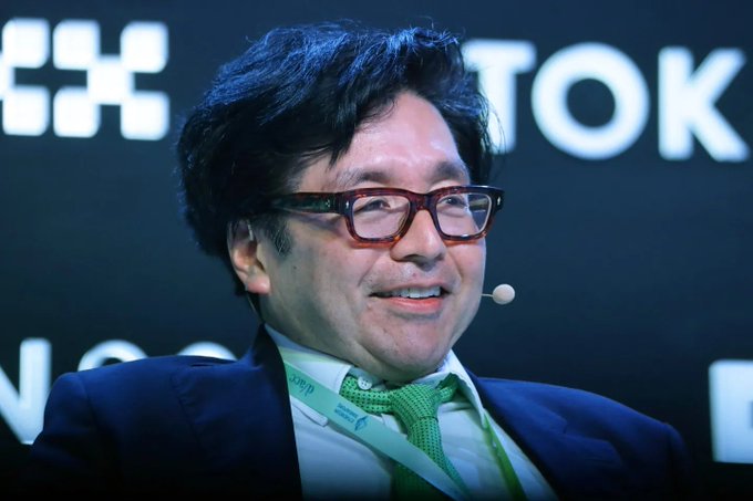 A man with glasses, a green tie, and a headset microphone smiles during what appears to be a conference, with partial text "TOKY" visible in the background. The image relates to the post by likely depicting Tom Lee, the fund manager behind Bitmine, whose company is aggressively accumulating Ethereum to reach a 5% supply target.