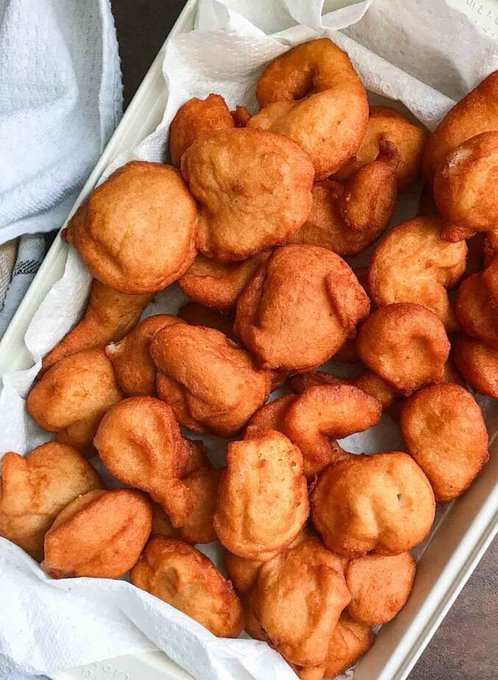 A tray filled with golden-brown, freshly fried dough pieces or fritters resting on white parchment paper.