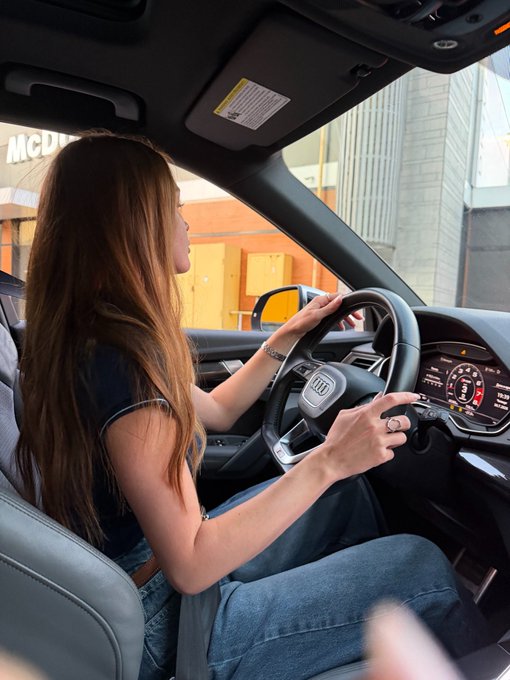 A woman sits in the driver's seat of an Audi, hands on the steering wheel, pulling out of a McDonald's parking lot. The visible "McD..." signage in the background plays on the joke in the post about leaving web3 to work at McDonald's, humorously implying the move to a fast-food job.