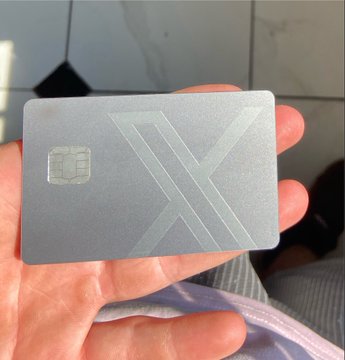 A hand holding a metallic gray card with a chip and a large 'X' design etched on its surface.