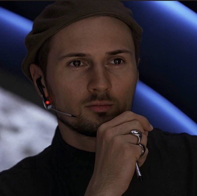 The image shows a man wearing a tan cap and a headset microphone, looking thoughtfully off-camera with his hand resting near his chin. He's wearing rings on his hand and appears to be at some kind of event or broadcast setting. This pairs well with the "GM & Happy New Month fam" post, possibly greeting followers with a contemplative, early morning vibe to start the new month.