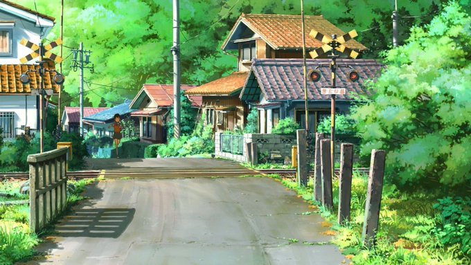 Anime-style artwork depicting a quiet, sunny street scene in a rural Japanese village with a railway crossing, green foliage, and traditional houses.