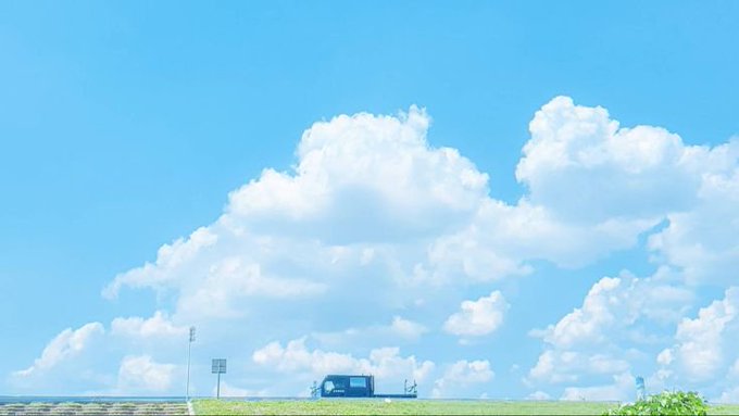 An animated landscape featuring a vast blue sky with large white clouds, a road, and a bus in the distance.