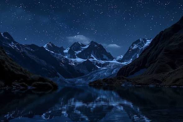 A serene nighttime landscape showing snow-capped mountains reflecting in a calm lake under a starry sky.