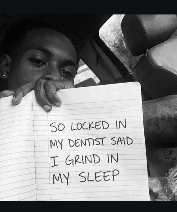 A black-and-white photo of a person in a car holding up a handwritten note that reads: 'SO LOCKED IN MY DENTIST SAID I GRIND IN MY SLEEP.'