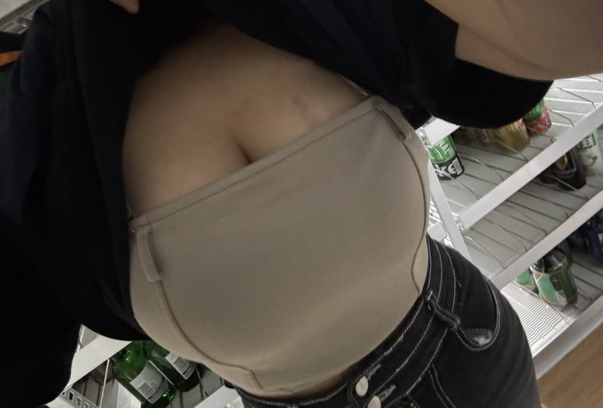 A close-up photo showing a person's lower back wearing a beige compression garment or shapewear, with a refrigerator containing drinks visible in the background.