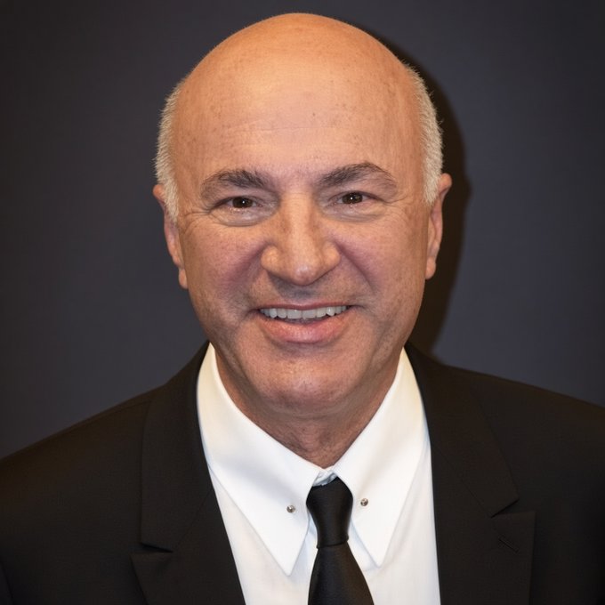 Kevin O'Leary, known as "Mr. Wonderful" from Shark Tank, smiles in a formal black suit and tie against a dark background. The portrait accompanies his comments about blockchain adoption and his crypto investment strategy following Ethereum's setback in securing major institutional partnerships.