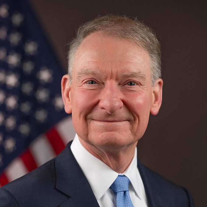 This image shows an older man with gray hair, wearing a dark suit, white shirt, and blue patterned tie, smiling in front of an American flag—appearing to be an official portrait likely associated with a U.S. official relevant to the post about the SEC's role in creating crypto regulations independently of Congress.