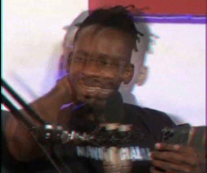 A smiling man with short hair wearing a dark shirt, appearing slightly blurry with a glitchy/vintage filter effect.