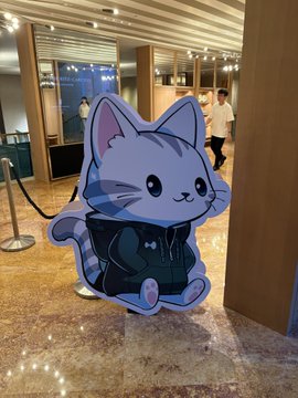 A cardboard cutout of a cartoon gray cat wearing a black hoodie stands on a polished floor in what appears to be a building lobby.