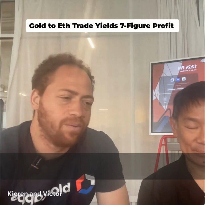 The image shows two men sitting next to each other with their faces close together. They are both wearing black t-shirts, one of which has a logo that reads "Kieren & Victor" written on it. The background features a white curtain and a poster or sign hanging behind the men.
