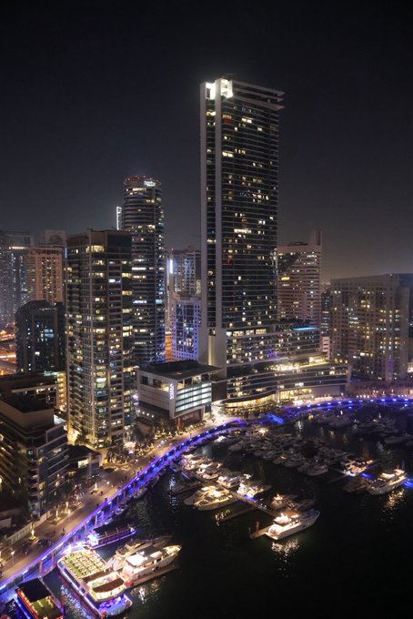 A nighttime aerial view of Dubai Marina showcases illuminated high-rise towers and a bustling harbor filled with docked yachts and boats. While the post references "GN" (good night), the image captures a vibrant city that clearly isn't sleeping, with glowing skyscrapers and waterfront lights creating a striking contrast to a typical "good night" sentiment.