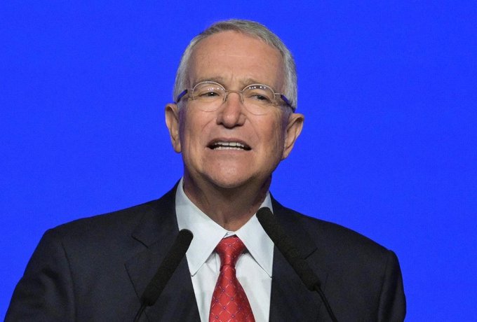 Ricardo Salinas Pliego, the billionaire behind Grupo Salinas, smiling while speaking at a podium against a blue backdrop. The image accompanies a post quoting his bullish prediction that Bitcoin would need to reach $1.86 million per coin to match gold's total market capitalization.