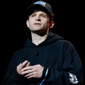 Jack Mallers, founder of Strike and a prominent Bitcoin advocate, speaks on stage wearing a black hoodie and a "Strike" branded cap. The image complements the post's quote highlighting his well-known preference for Bitcoin over the US dollar.