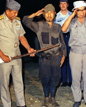 A historical photo showing two military officers flanking a disheveled soldier in tattered clothing who is saluting, with another soldier in the background.