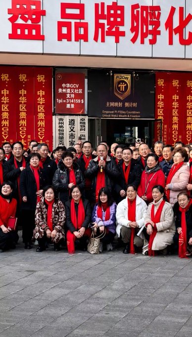A large group photo of people wearing red scarves gathered outside a building with Chinese signage, including banners celebrating '中华区贵州CZY' and text about 'P2i2Day Countdown' and 'Empower in P2iDay Countdown Unlock Web3 Wealth & Freedom'.