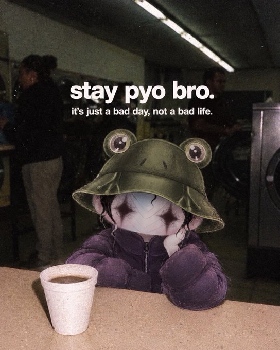 A sad frog plushie wearing a frog bucket hat and purple hoodie sits at a table with a cup of coffee in a dimly lit room, with text reading 'stay pyo bro. it's just a bad day, not a bad life.'