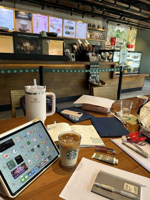 A Starbucks coffee table scene shows an iPad, iced coffee, a Stanley tumbler, and planner surrounded by empty seating, mirroring the post's message about finding opportunity in quiet, overlooked moments before a bull run begins. Menu boards in the background advertise "Featured" items and "Top 1% Arabica Coffee Beans."