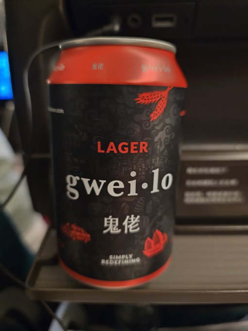 A black and red can of 'gwei·lo LAGER' beer features Chinese characters (鬼佬) and the tagline 'SIMPLY REDEFINING', resting on a surface near a coffee machine.